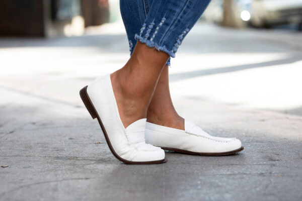 Pantofi albi tip loafer purtați pe trotuar urban